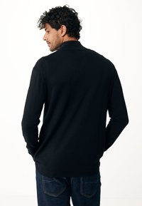 Polo shirt nero a maniche lunghe in un materiale a maglia liscia, caratterizzato da un colletto e una silhouette aderente, abbinato a jeans scuri.