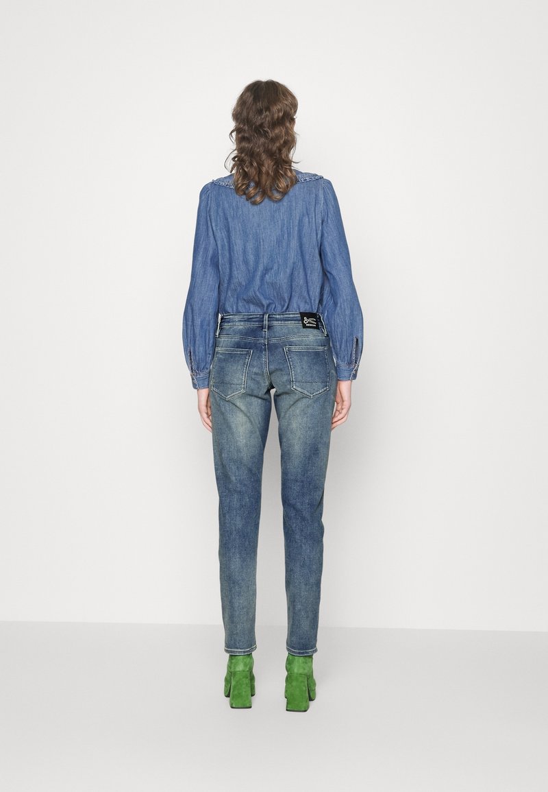 Jean en denim avec une finition bleu délavé et une coupe slim. Associé à une chemise chambray à manches longues, avec un col texturé et des talons verts.