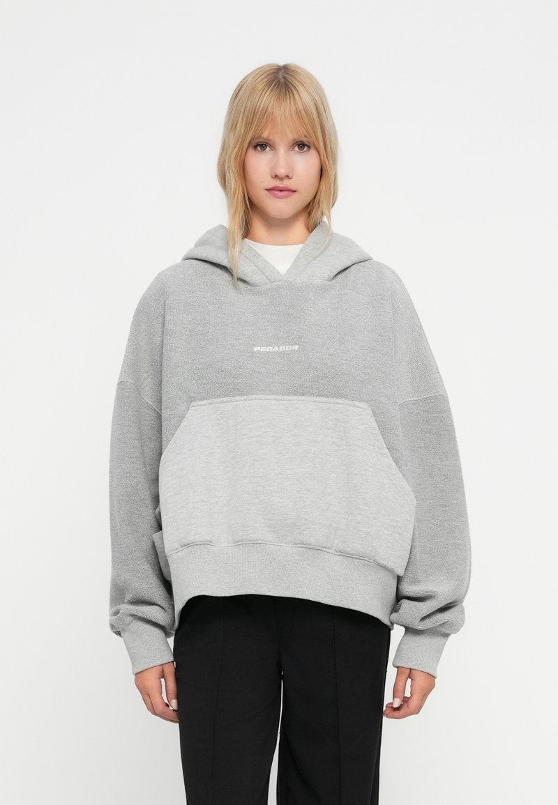 Pilkas per didelis hoodie, pagamintas iš minkštos medvilnės mišinio, su priekyje esančia kengūros kišene ir gumbuotomis rankovėmis, ant krūtinės yra "PEGADOR" logotipas.