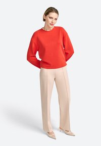 Rode sweatshirt met een ronde hals, losse pasvorm en lange mouwen, gecombineerd met beige uitlopende broek met verticale stiklijnen.