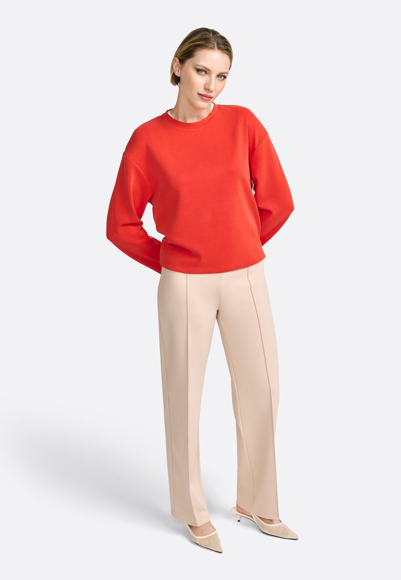 Rode sweatshirt met een ronde hals, losse pasvorm en lange mouwen, gecombineerd met beige uitlopende broek met verticale stiklijnen.