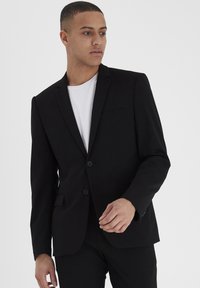 Blazer negro de tela suave, con un diseño estructurado, cierre de un solo botón, solapas en pico y dos bolsillos frontales.