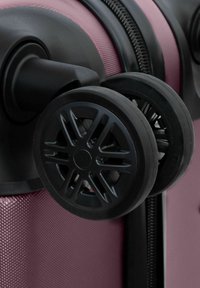 Hartschalentrolley in Pink mit texturierter Oberfläche, ausgestattet mit zwei schwarzen Rädern mit detailliertem Speichen-Design und einem stabilen schwarzen Griff.