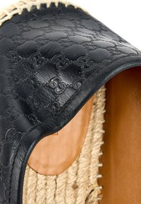 Gros plan sur une tige de chaussure en cuir noir avec motif GG entrelacé embossé et bordure de semelle en jute tissée.