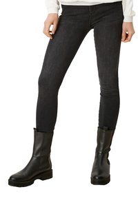 Jeans negros ajustados combinados con botas de cuero negras hasta el tobillo. Las botas tienen una suela baja y robusta y un diseño minimalista.