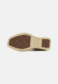Sole din cauciuc maro cu un model geometric de profil, intermediar bej și branding subtil. Baza este concepută pentru aderență și durabilitate.