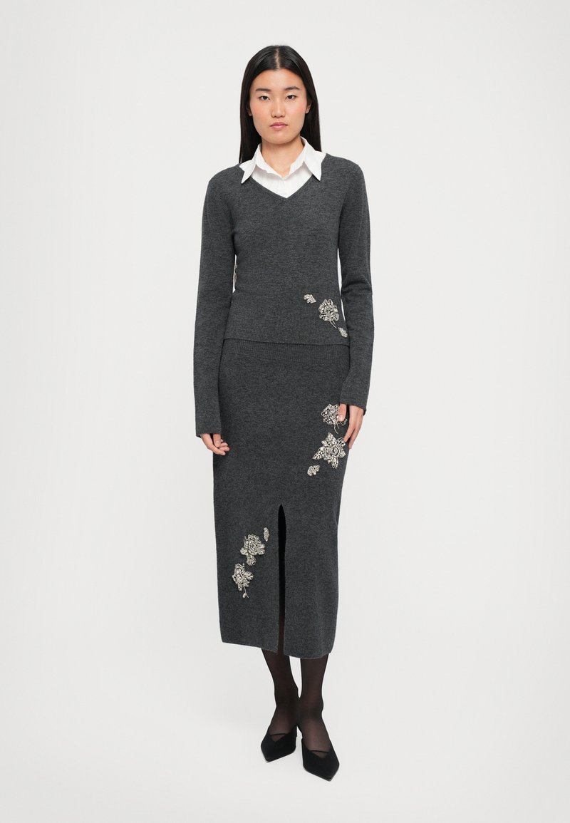 Pull en maille grise avec col en V et manches longues, associé à une jupe crayon assortie dotée d'une fente devant et d'ornements floraux.