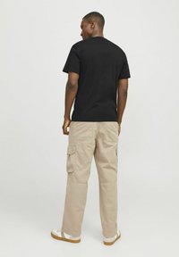 Zwarte katoenen T-shirt gecombineerd met beige cargobroek. De broek heeft zijzakken en een relaxte pasvorm. Schoenen zijn wit met bruine zolen.