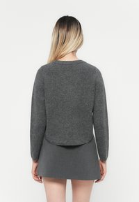 Grå ullgenser med en avkortet silhuett, lange ermer og en rund halslinning. Brukt over et grått minis skjørt. Myk tekstur.