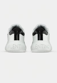 Baskets blanches avec un accent noir brillant sur le talon, présentant un dos texturé avec "VALENTINO" en relief pour le détail.