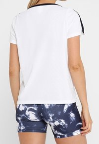 Valkoinen lyhythihainen t-paita, jossa on tummansininen reunus, yhdistetty sinisiin tie-dye-kuvioituihin shortseihin, joissa on valkoisia spiraalikuoseja ja joustava vyötärö.