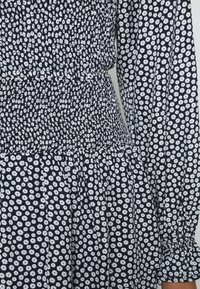 Námořnické šaty s bílým květinovým vzorem, nařaseným pasem a dlouhými rukávy s nabranými manžetami. Lehká látka s texturovaným povrchem.