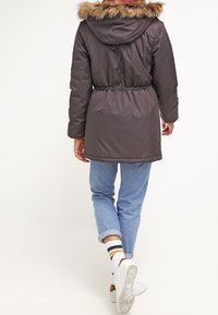 Dark gray parka with faux fur hood, elastic waist, and cinched cuffs, paired with light blue rolled jeans and white sneakers.