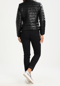 Svart quiltad puffjacka med ståkrage, i kombination med svarta jeans och silvriga sneakers. Jackan har en slät, glansig yta.