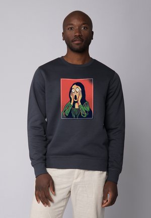 Marineblaues Sweatshirt mit einer Illustration einer Person mit weit geöffneten Augen und Händen im Gesicht, vor einem roten Hintergrund.