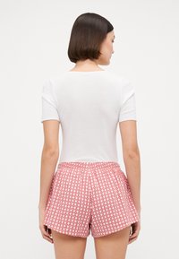 Hvit kortermet topp kombinert med røde rutede shorts med et hvitt rutenettmønster og elastisk midjebånd, sett bakfra.