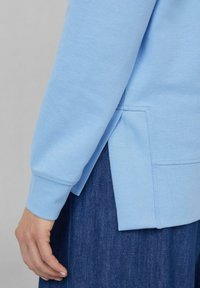 Felpa azzurra realizzata in tessuto morbido, con maniche lunghe e dettagli di apertura laterale. Abbinata a un materiale in denim blu scuro.