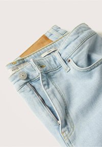 Light blue denim jeans with a front zipper, button closure, and leather patch. Features contrast stitching and brand labels inside the waistband.