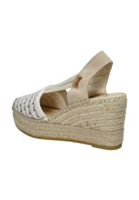 Sandalo con zeppa caratterizzato da una tomaia intrecciata color crema con dettagli neri, un retro in suede color beige chiaro e una suola in corda di juta naturale. Include cinturino elastico alla caviglia.