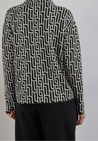 Maglione a righe bianche e nere con un design geometrico. Texture morbida, maniche lunghe e vestibilità rilassata. Colore di base nero con accenti bianchi.