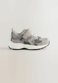 Szare i beżowe sneakersy dziecięce z siateczkowej tkaniny, zamszowymi detalami, białą podeszwą, czarnym bieżnikiem, sznurówkami oraz paskiem na rzep na jasnym tle.