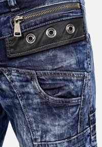 Jeans di denim con una finitura blu consumata, un design di tasche classico e un accento in pelle nera con occhielli argentati e una cerniera.