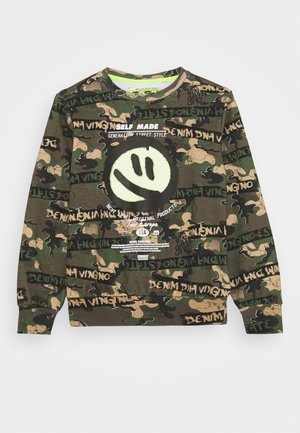 Bluza w wzór camo w odcieniach zieleni, brązu i czerni, z dużym uśmiechniętym wzorem, grafiką oraz ściągaczami przy mankietach i u dołu. Miękka tekstura.