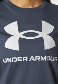 Mörkblå bomulls-T-shirt med en stor vit logotyp som har stiliserade "U" och "A" ovanför orden "UNDER ARMOUR" i fet vit text.