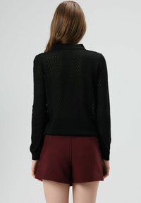 Zwart, trui met een diamantpatroon, lange mouwen en een kraag, gecombineerd met bordeauxrode shorts met hoge taille.