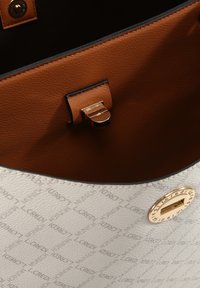 Weißes strukturiertes Handtaschen-Innenleben mit braunen Lederelementen, einem goldenen Verschluss und prägierten Logomuster. Verfügt über einen magnetischen Druckverschluss.
