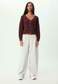 Bordeauxrotes Cropped-Sweatshirt mit Knöpfen, kombiniert mit hellgrauen, weit geschnittenen Sweatpants und weißen Sneakers. Die Textur ist gewoben und weich.