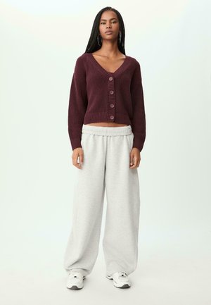 Bordeauxrotes Cropped-Sweatshirt mit Knöpfen, kombiniert mit hellgrauen, weit geschnittenen Sweatpants und weißen Sneakers. Die Textur ist gewoben und weich.