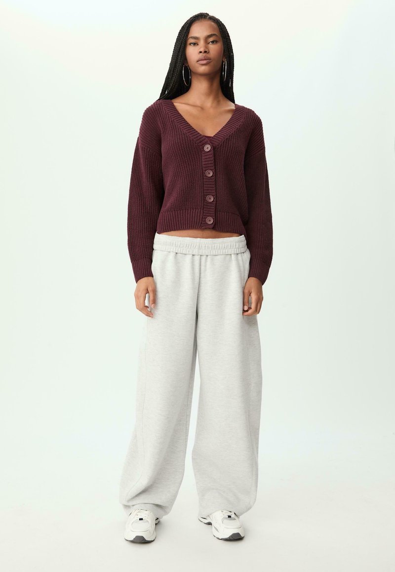Bordeauxrotes Cropped-Sweatshirt mit Knöpfen, kombiniert mit hellgrauen, weit geschnittenen Sweatpants und weißen Sneakers. Die Textur ist gewoben und weich.