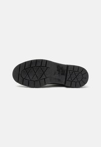 Suela de bota de goma negra con acabado texturizado y profundas ranuras para un mejor agarre. Presenta una marca destacada y un diseño resistente para mayor durabilidad.