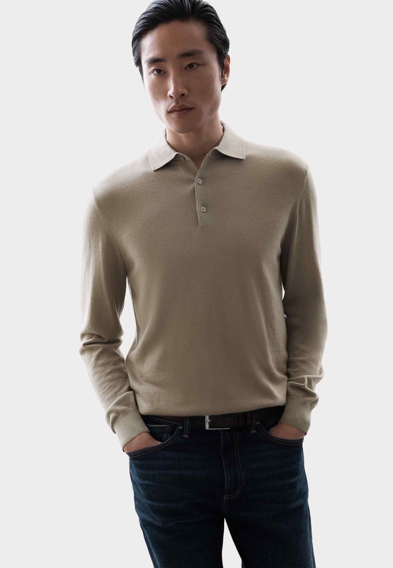 Krémová polokošile s dlouhým rukávem a dvojitým knoflíkem na límci, spárovaná s tmavými džínami. Minimalistický design, jemná textura.