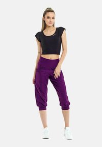 Sort cropped top med korte ærmer, parret med lilla, baggy bukser til midt på læggen, der har lommer og elastisk talje, båret med hvide sneakers.