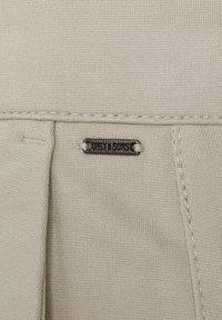 Tessuto a maglia beige con un piccolo etichetta metallica cucita sopra, incisa con il nome del marchio "Only & Sons."