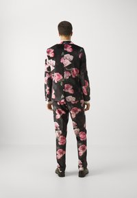 Floral suit in black fabric, adorned with large pink and white rose patterns. Features a tailored fit, notched lapel, and matching trousers.