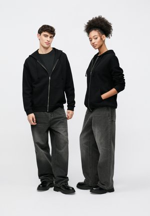 Fekete, elöl cipzáros kapucnis pulóverek elülső zsebekkel, sötét ingek fölött viselve. Mindkét személy széles szárú szürke farmert és masszív fekete cipőt hord. Egyszerű, hétköznapi öltözék.