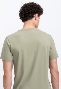Olijfgroene katoenen t-shirt met een ronde hals, korte mouwen en een subtiele schaarlogo geborduurd op de achterkant van de nek.