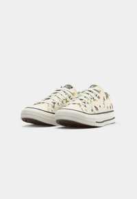 Low-top white canvas sneakers with small purple and orange floral patterns, white laces, and rubber soles on a plain background.
