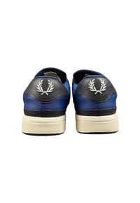 Un paio di sneaker blu e nere con il logo bianco a forma di alloro sui talloni e suole off-white, viste da dietro su sfondo bianco.