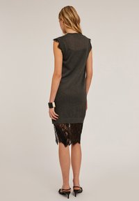 Rochie tricotată gri fără mâneci, cu o margine din dantelă ce se extinde mai jos, având detalii texturate la umeri și un accent modern din bijuterii negre.
