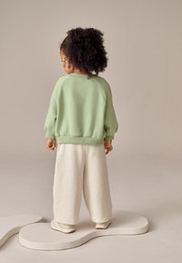 Jasnozielony sweatshirt z raglanowymi rękawami, w połączeniu z przejrzystymi, kremowymi spodniami o szpiegowatej fakturze, noszonymi z białymi butami.