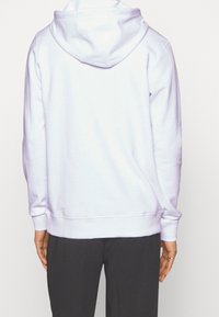 Weiße Kapuzenjacke mit Kordelzug, gerippten Bündchen und lässiger Passform. Weiche Textur mit glatter Oberfläche, getragen über schwarzen Hosen.