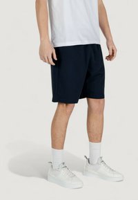 Pantaloni sportivi blu navy realizzati in un tessuto morbido, dotati di una vita elastica. Abbinati a sneakers bianche e calze bianche a coste.