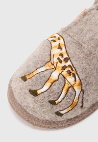 Zapatilla gris de felpa con un diseño bordado de jirafa en amarillo y marrón, con patrones detallados en las patas y una forma suave y redondeada.