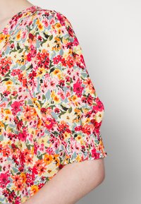 Blusa floral com mangas curtas e bufantes; apresenta um padrão floral multicolorido vibrante sobre um fundo claro; punhos das mangas elásticos.