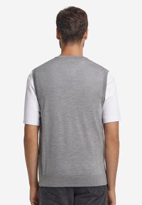 Grå ärmlös tröja i mjukt material med ribbad fåll, lagd ovanpå en vit kortärmad skjorta. Enkel och neutral design.