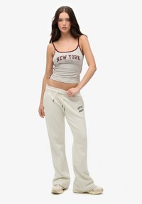 Grijze, getailleerde tanktop met "NEW YORK" in bordeauxrode tekst; gecombineerd met losse, crèmekleurige joggingbroek met een gedrukt logo; beige sneakers.